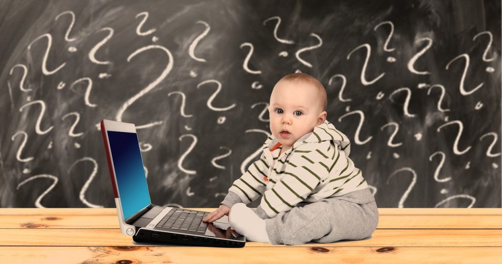 ノートパソコンのキーボードを不思議そうに打つ赤ちゃん